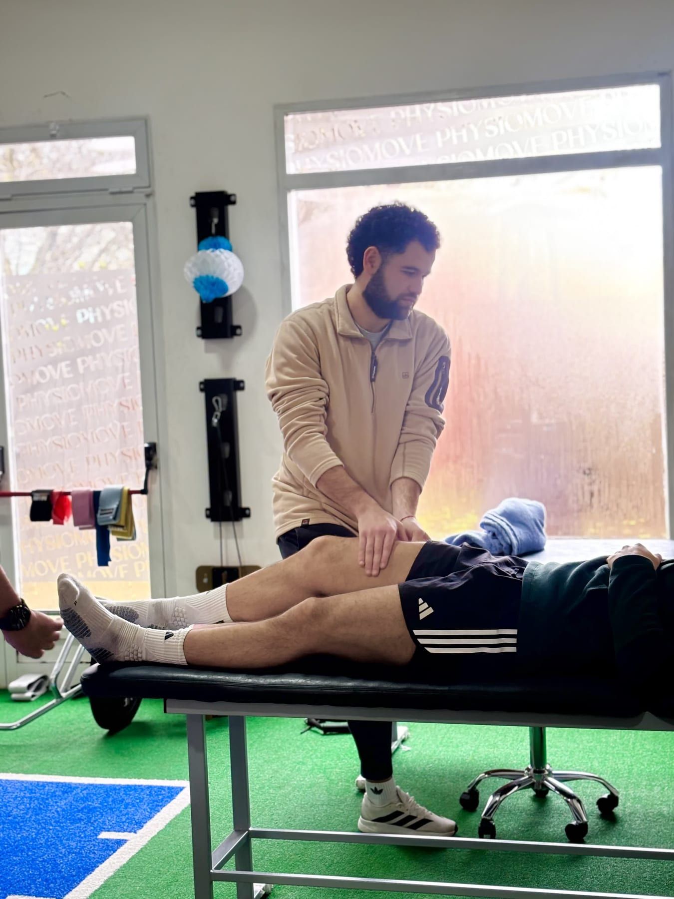 Kinesiólogo de PhysioMove evaluando la rodilla de un paciente recostado en la camilla del box