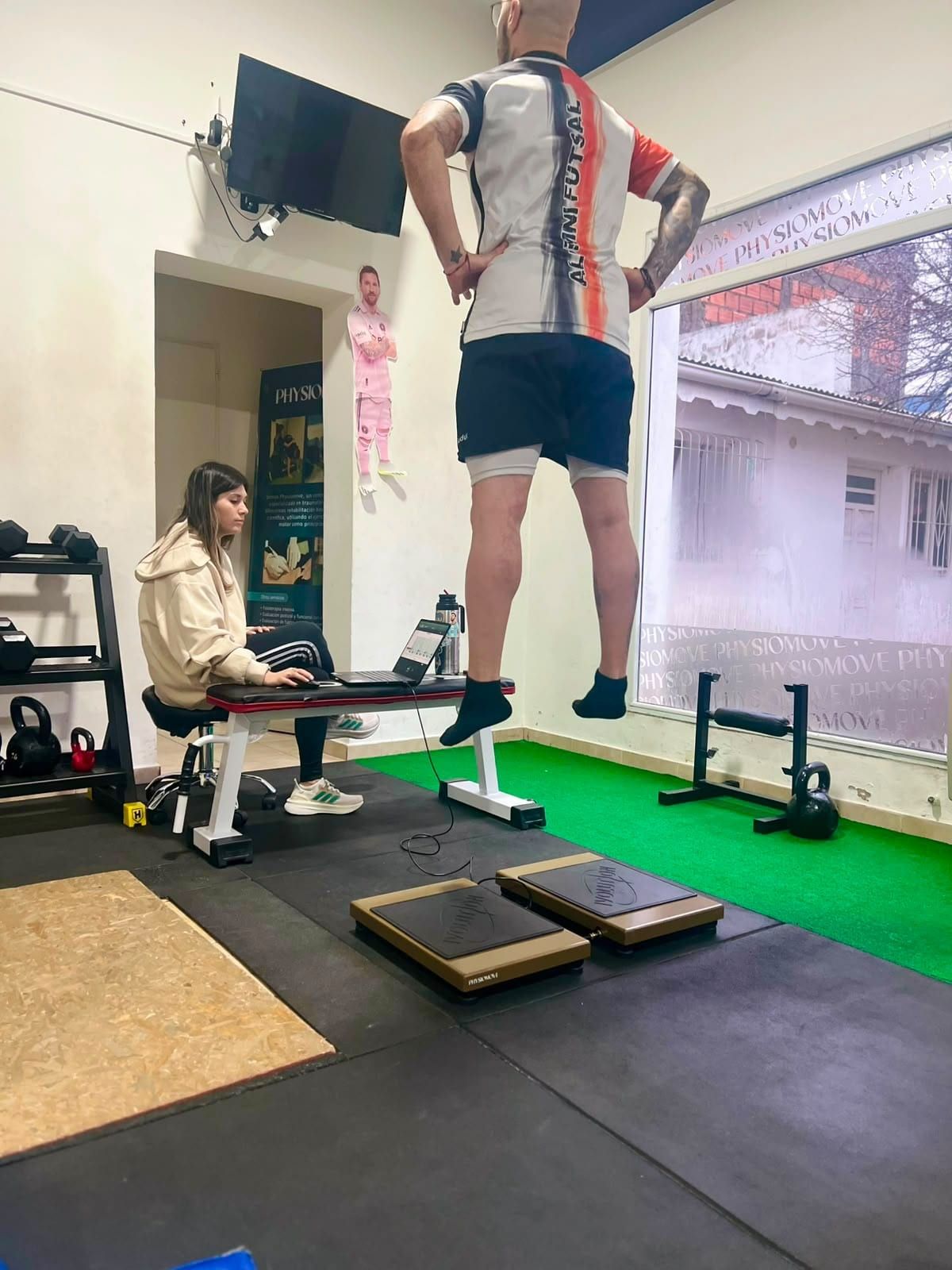 Deportista en el aire durante un test de salto sobre las plataformas de fuerza IVOLUTION, mientras una kinesióloga de PhysioMove sigue los datos en la laptop